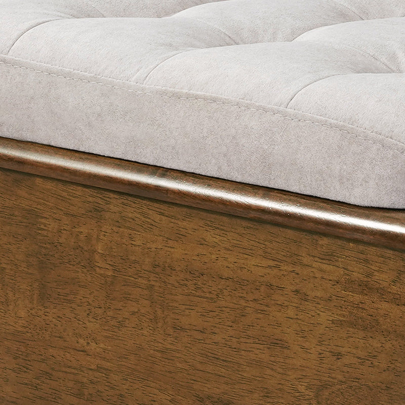 A close-up view of the smooth wooden frame and soft gray tufted fabric cushion of an ottoman footstool.