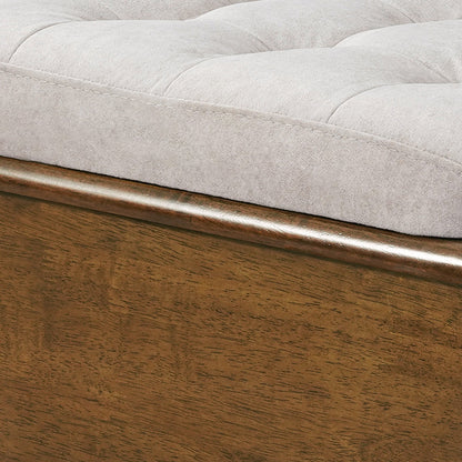 A close-up view of the smooth wooden frame and soft gray tufted fabric cushion of an ottoman footstool.