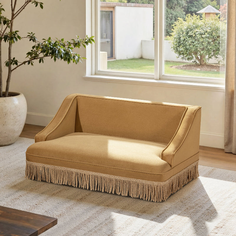 A three-quarter angle view of a vintage mustard yellow velvet cat sofa bed featuring a button-tufted backrest and dangling fringe trim on a white background.