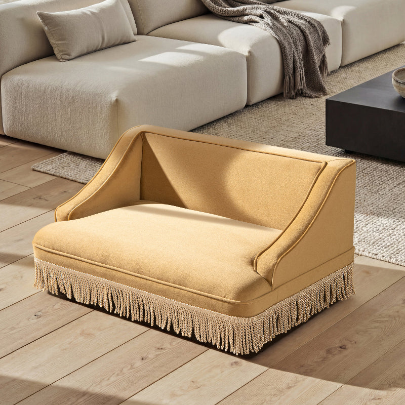 An elevated view of a vintage mustard yellow cat sofa bed with tassel fringes placed on a hardwood floor in a modern living room.