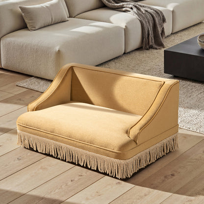 An elevated view of a vintage mustard yellow cat sofa bed with tassel fringes placed on a hardwood floor in a modern living room.