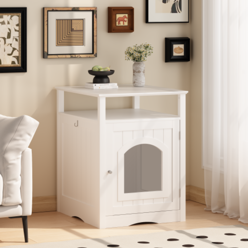 A white wooden cat litter box enclosure styled as a side table in a cozy room corner, topped with decorative items and an open shelf.