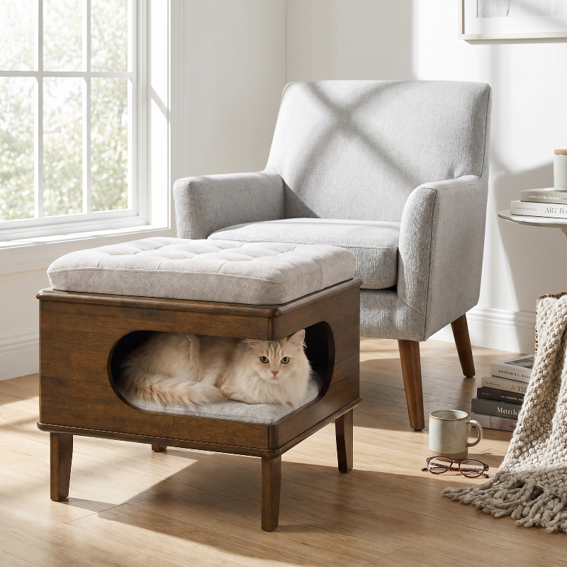 A fluffy long-haired white cat resting comfortably inside a wooden ottoman footstool with a gray tufted cushion on top.